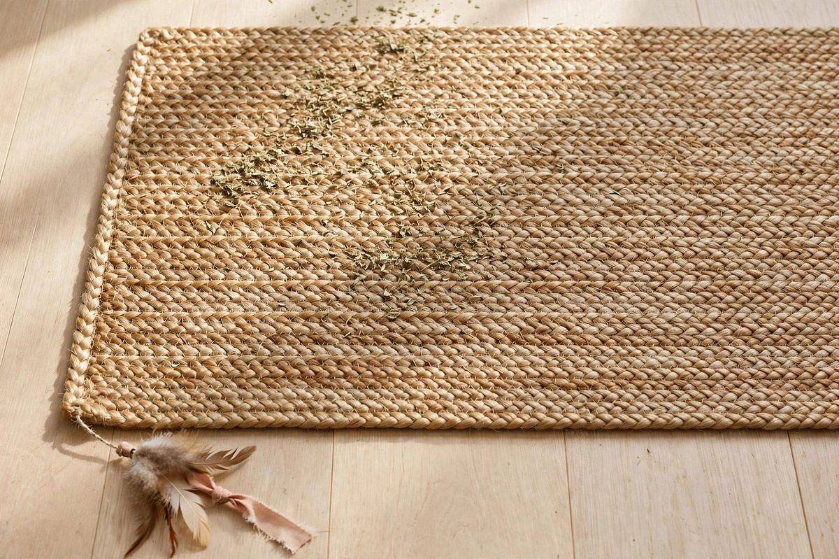 Flat sisal and jute cat scratching mat with feather ribbon toy and catnip on a wooden floor